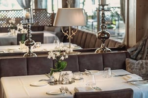 A dining area with tables set for service, featuring a vase of flowers, a lamp, and a view through the window.