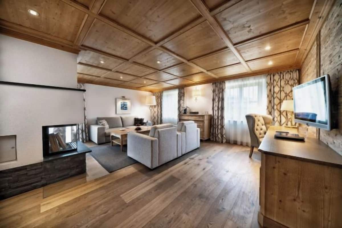 Ein geräumiges Wohnzimmer mit Holzbalkendecke, Kamin, einer Sofagarnitur, einem Fernseher und einem Essbereich.