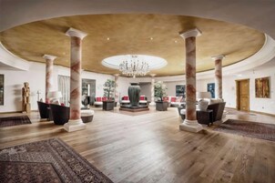 A spacious lobby with a high ceiling, marble columns, and a central chandelier.