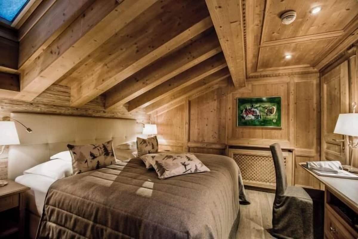 Ein holzgetäfeltes Zimmer im Chalet-Stil mit einem Bett, einem Schreibtisch und einem Sessel.