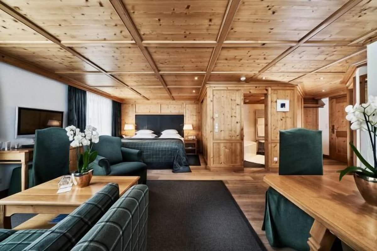 Ein gemütliches Zimmer mit Holzbalkendecke, einem Bett, einem Schreibtisch und einer Sitzecke.