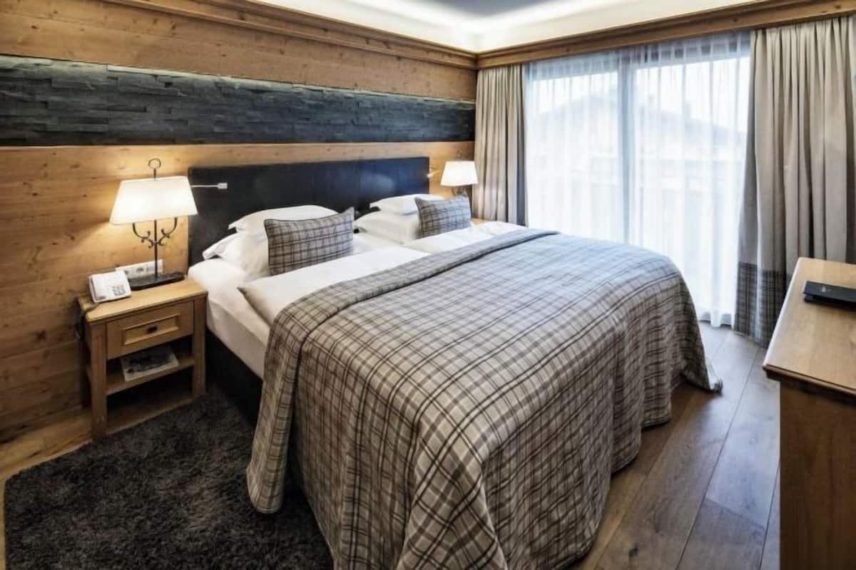 Ein Hotelzimmer mit einem großen Bett, Holzwänden, einem Nachttisch mit Lampe und Blick ins Freie durch ein Fenster.