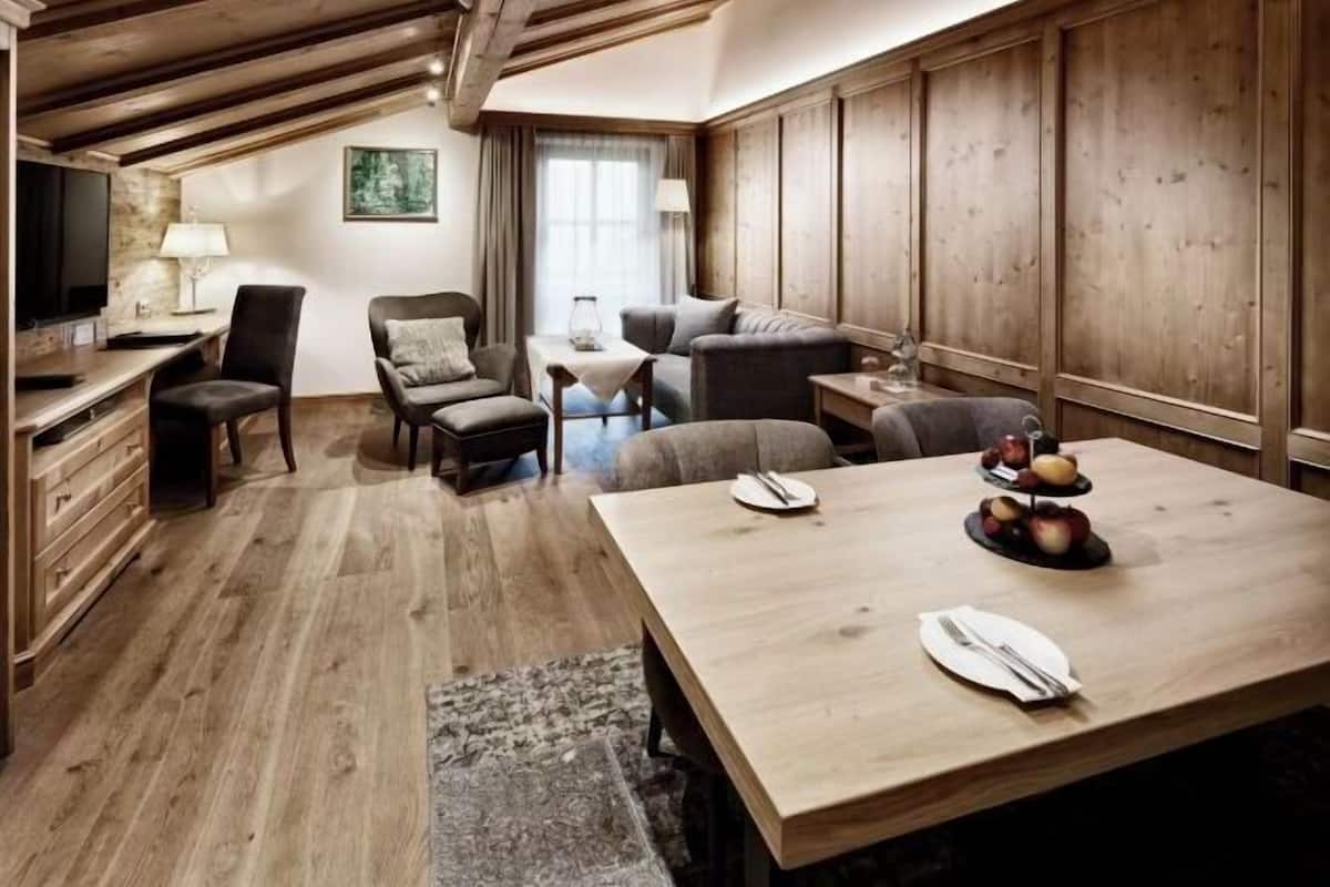 Ein gemütliches Zimmer mit Holzboden, einem großen Tisch mit Obstschale und einem Fernseher links.