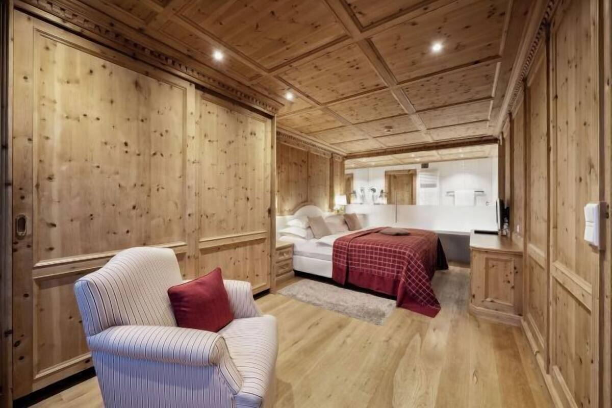 Ein Zimmer mit Holzwänden, einem gestreiften Sessel, einem Bett mit roter Decke und einem Nachttisch.