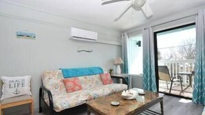 A room with a sofa, a small table, an air conditioning unit, and a view of the outside. - Condo 224 Beautiful Cedar key (Cedar Key)