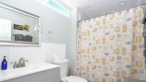A bathroom with a white sink, a toilet, a mirror, and a shower curtain with a pattern. - Condo 224 Beautiful Cedar key (Cedar Key)