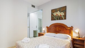 A hotel room with a large bed, two bedside tables with lamps, a wooden headboard, a painting of flowers on the wall, and a bathroom visible through an open door.