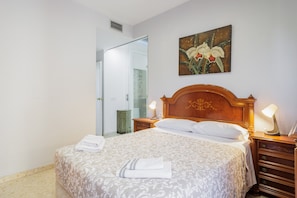 A hotel room with a large bed, two bedside tables with lamps, a wooden headboard, a painting of flowers on the wall, and a bathroom visible through an open door.