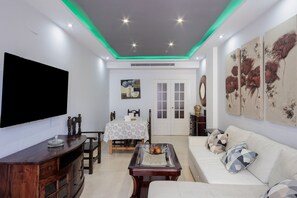Un salon doté d’un téléviseur à écran plat, d’un meuble de rangement en bois, d’un canapé et d’œuvres d’art accrochées aux murs.