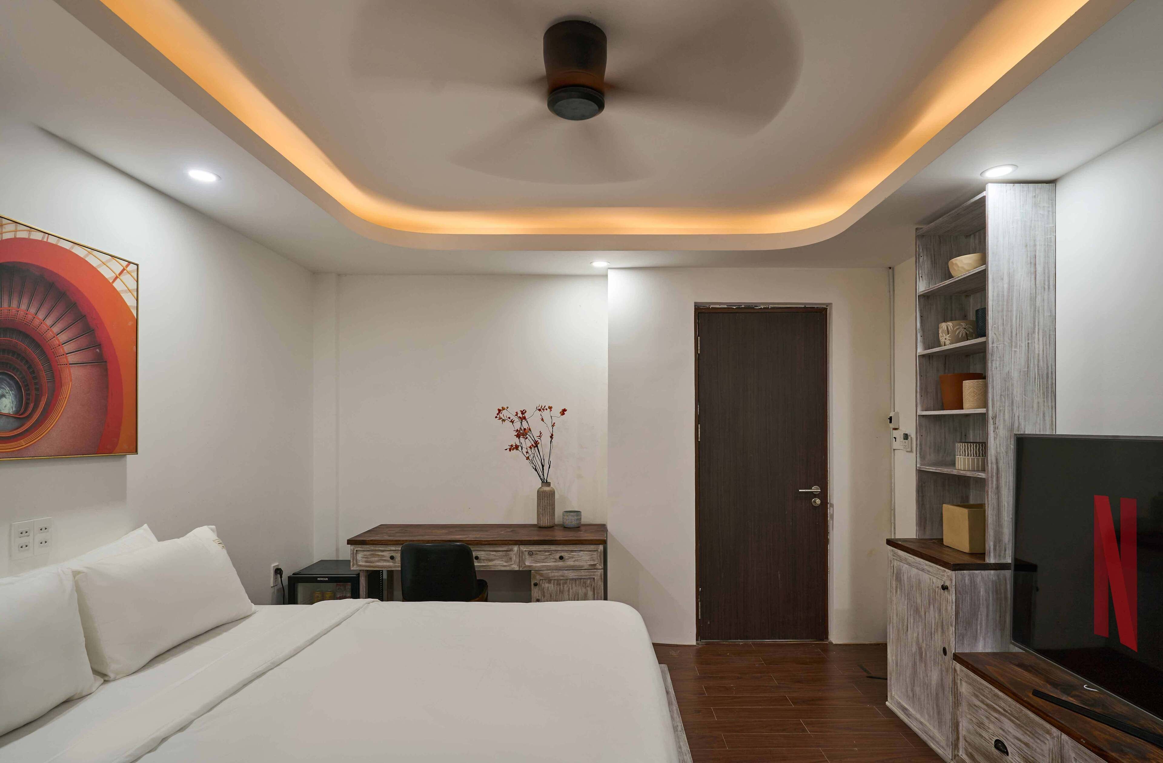 A hotel room with a bed, desk, TV, and a door.
