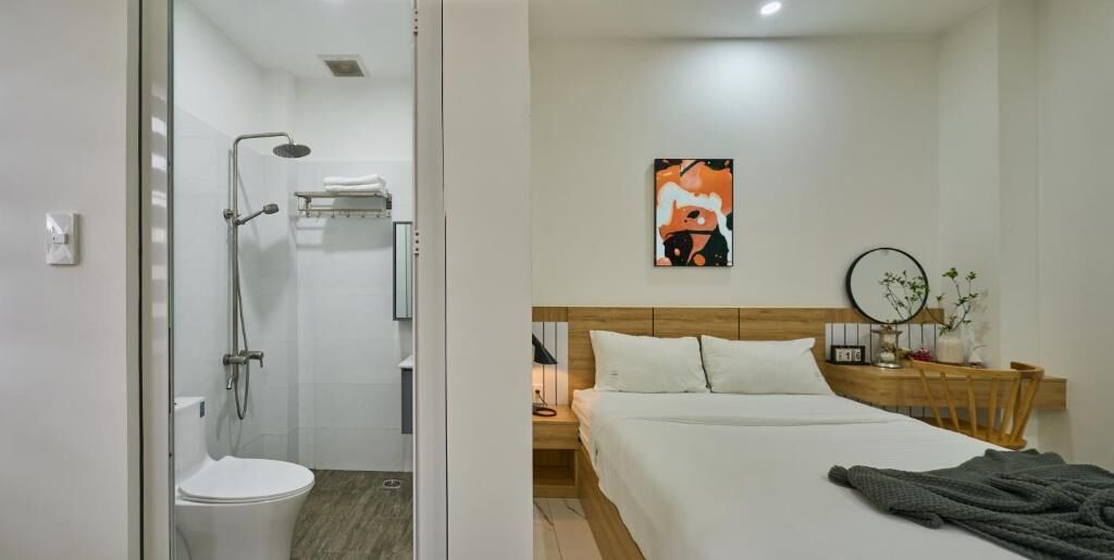 A hotel room with a shower, toilet, bed, bedside table, and a wall-mounted artwork.