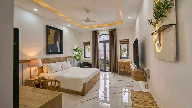 A modern hotel room with a large bed, a desk, a chair, a TV, and a balcony with curtains. - Green Riverside Hotel (Ho Chi Minh City)