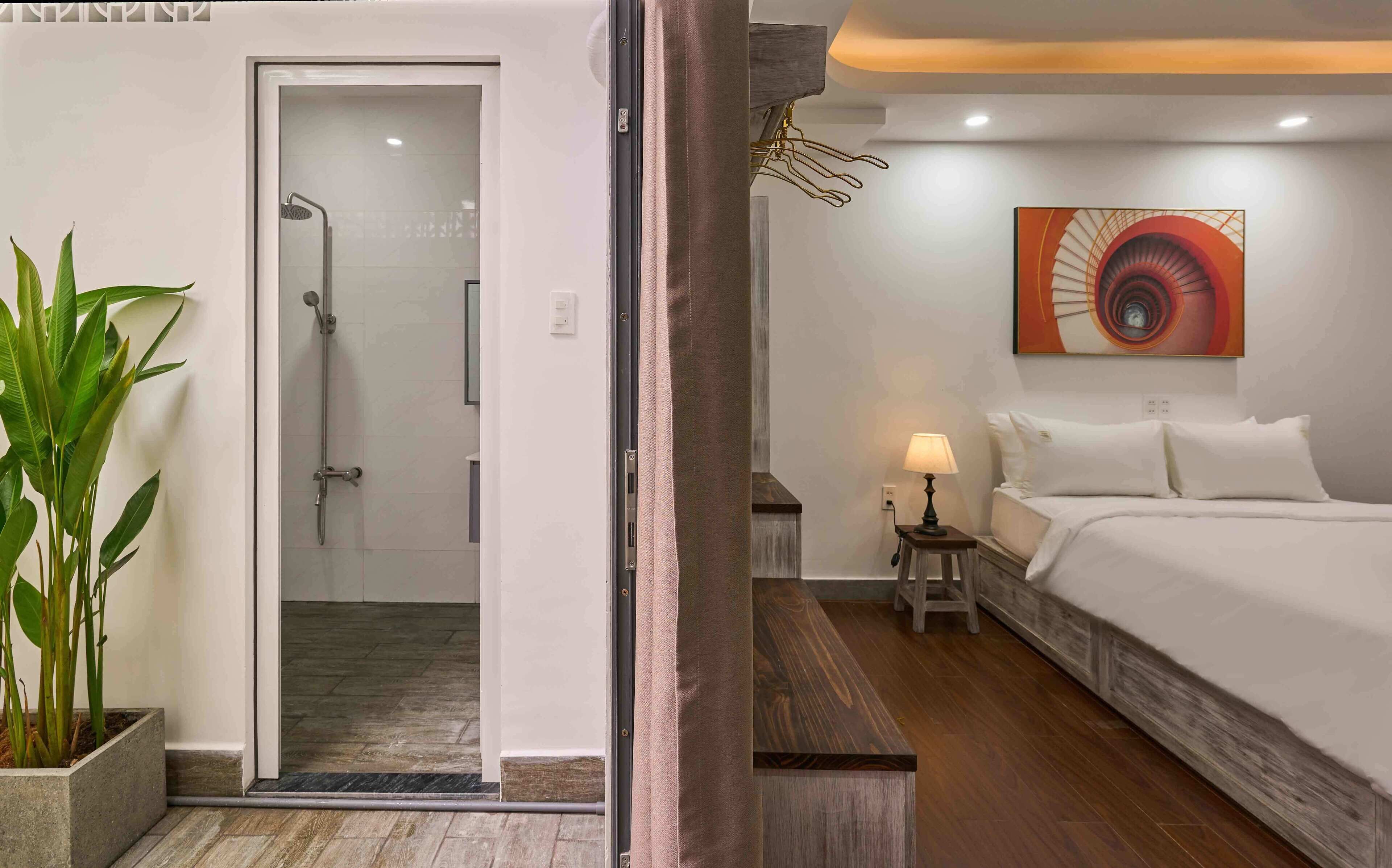 A hotel room with a bed, bedside table, lamp, and a painting on the wall.