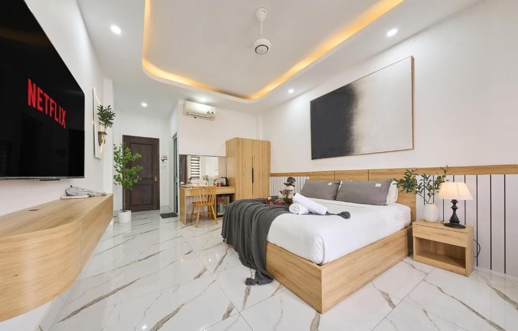 Habitación de hotel moderna con cama de madera, un escritorio, una silla, un televisor y una recepción.