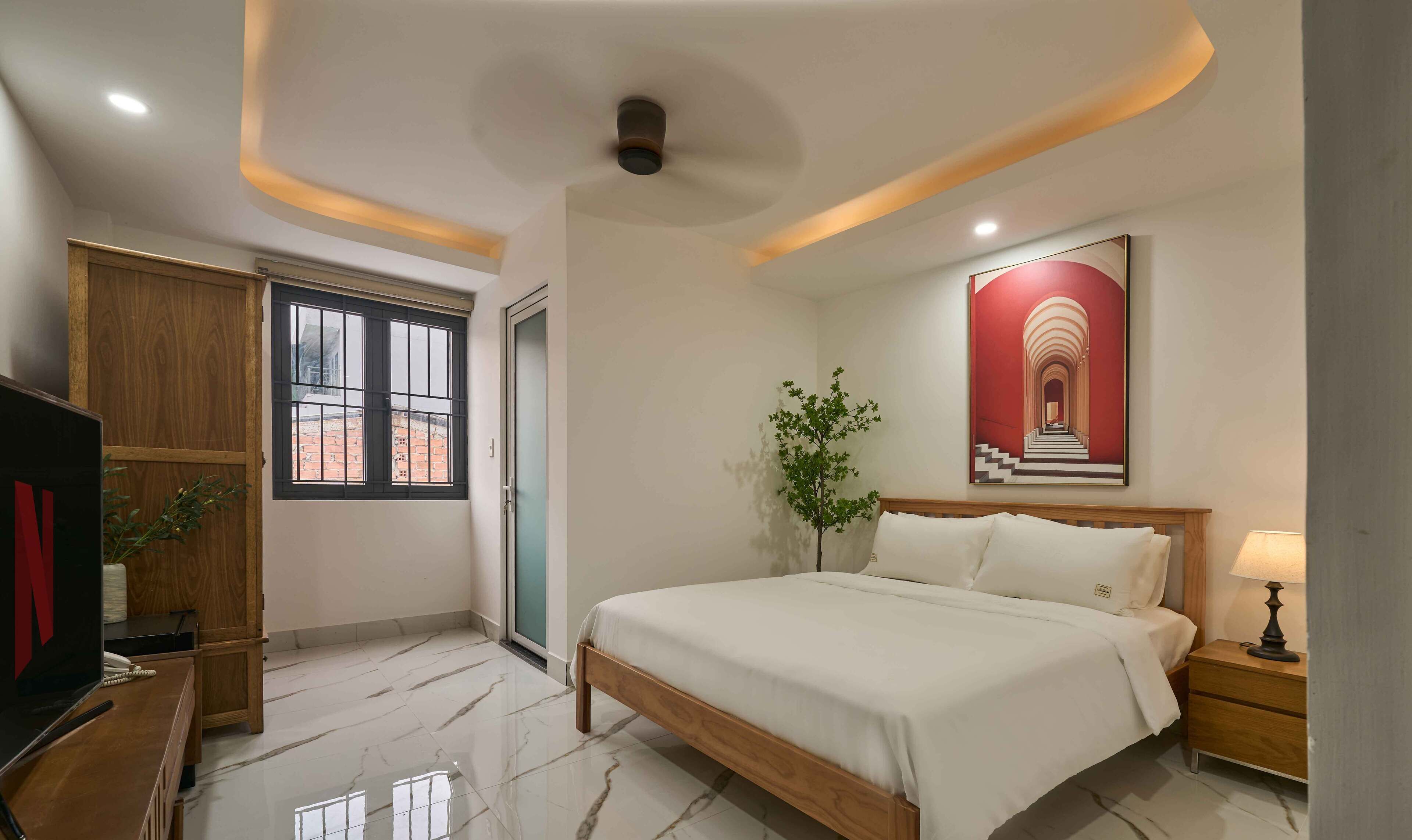 Un dormitorio con cama, mesita de noche, lámpara y un cuadro en la pared.