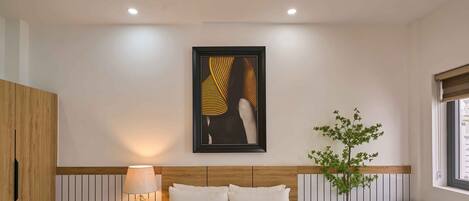 Une chambre à coucher moderne avec un grand lit, une lampe de chevet, une œuvre d’art encadrée, une plante en pot et un fauteuil en cuir.