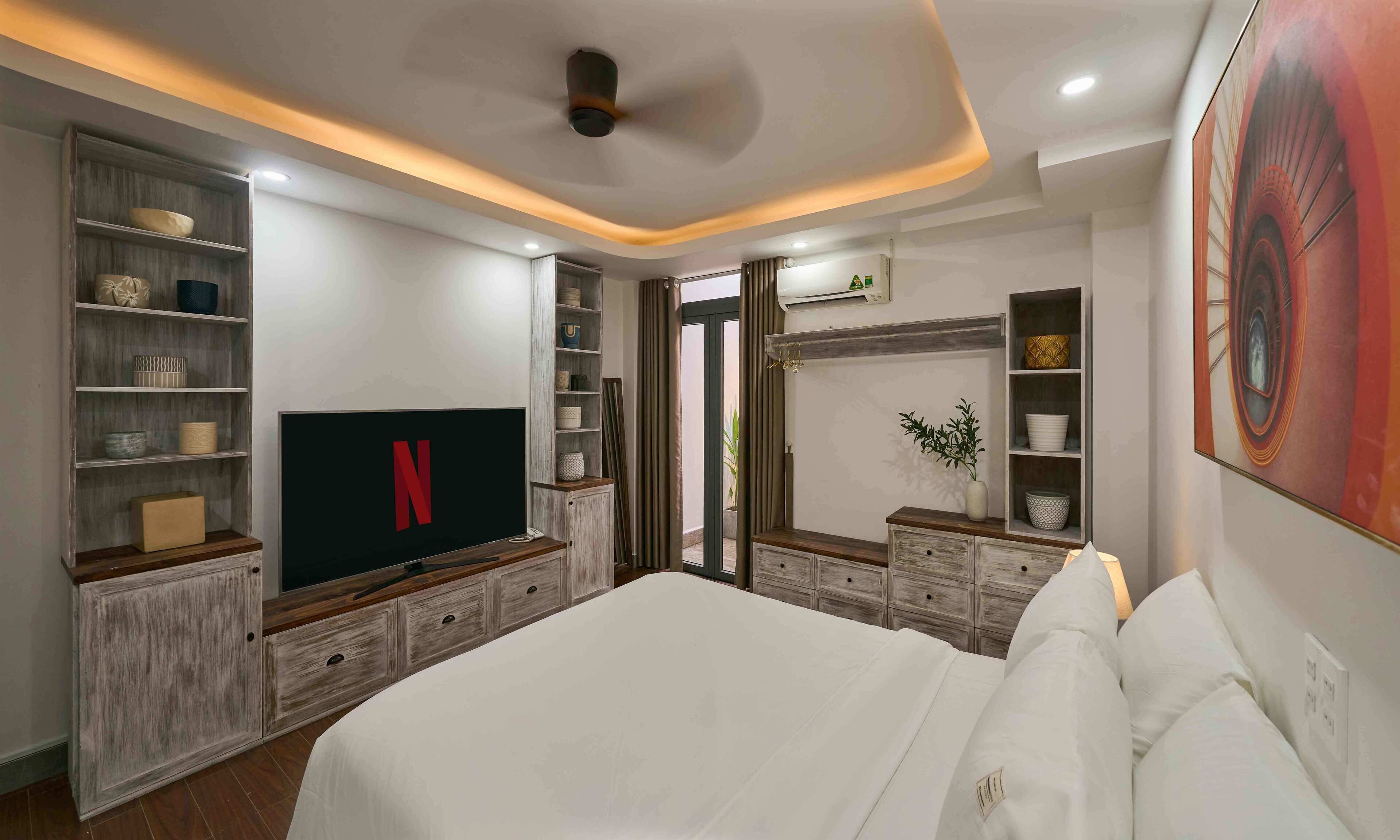 A bedroom with a large bed, built-in shelving with decorative items, a flat-screen TV, and a ceiling fan.