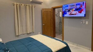 Una camera da letto con un letto, tende, un ventilatore a soffitto, un condizionatore d'aria e una TV che mostra un programma.