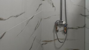 Doccia con soffione a mano e tubo flessibile, montati su una parete con motivo marmorizzato.