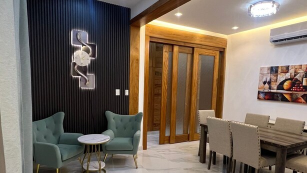 Un soggiorno moderno con divano, poltrone, tavolo da pranzo e un elemento decorativo a parete.