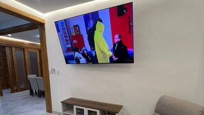 Un soggiorno moderno con una televisione a schermo piatto montata al muro, un divano beige, un tavolino da caffè bianco e un mobile TV in legno.