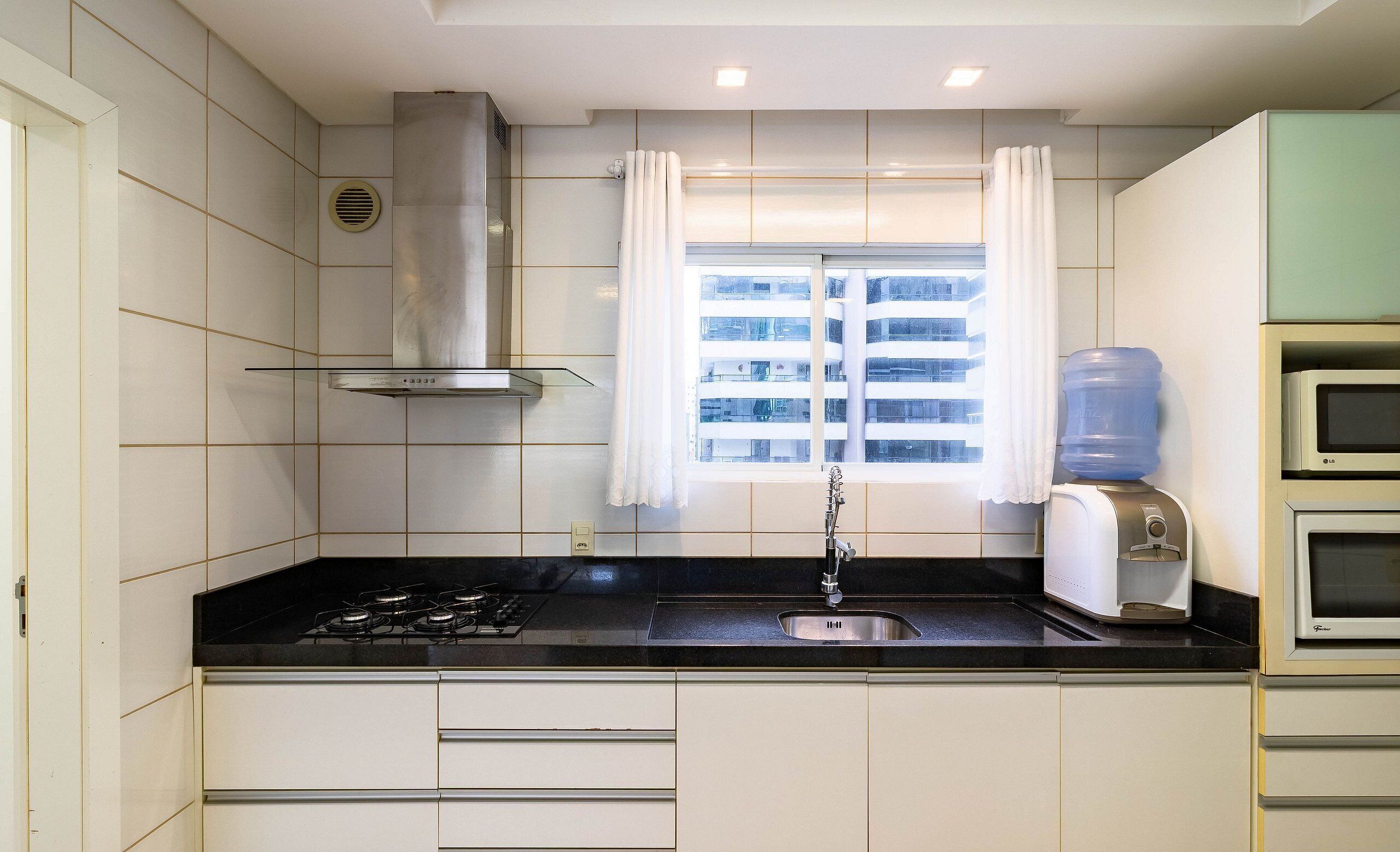 A kitchen with a gas stove, a sink, a water dispenser, and a window with curtains.