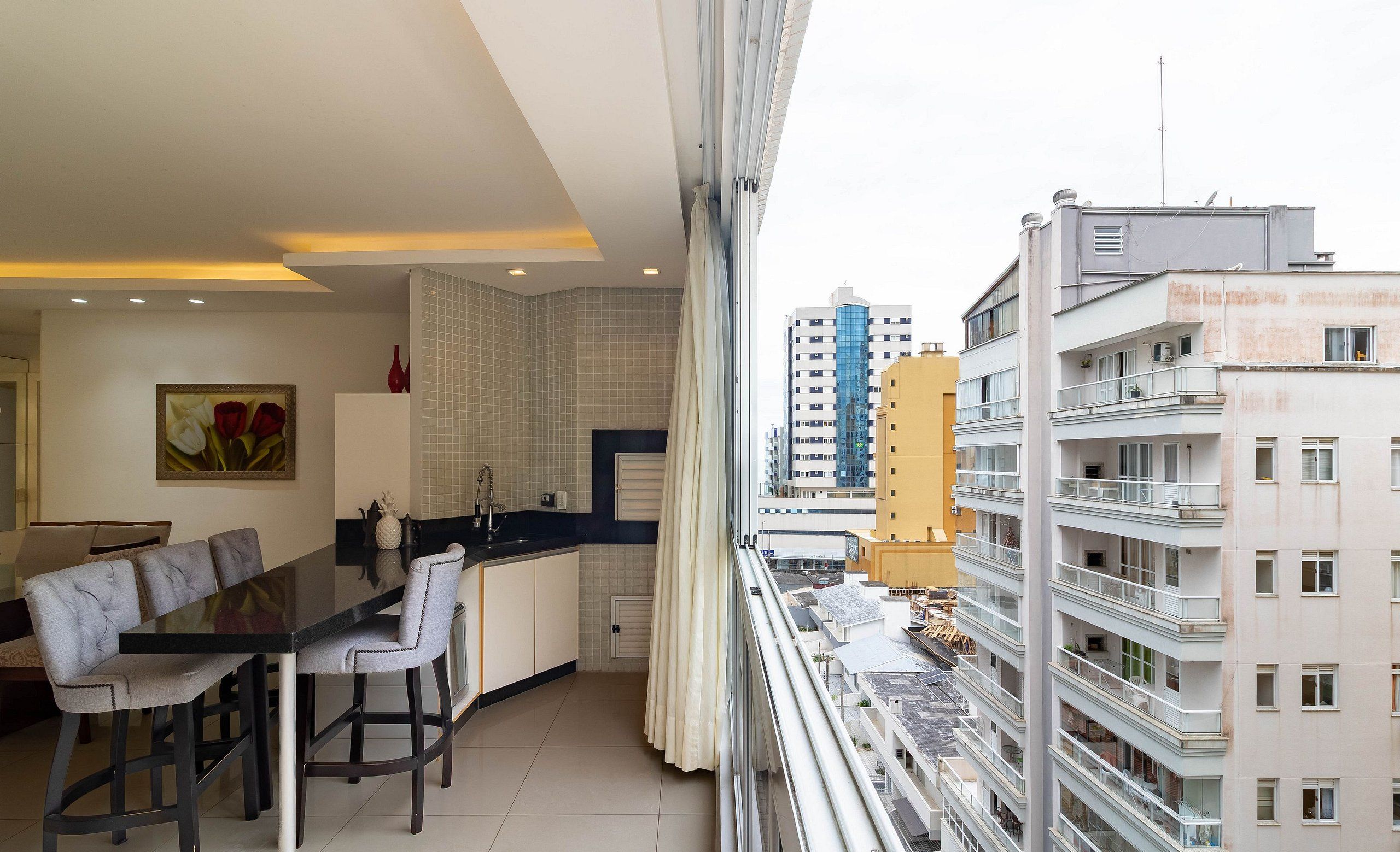 A modern apartment with a dining area, kitchen, and large windows overlooking a cityscape.