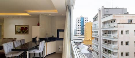 A modern apartment with a dining area, kitchen, and large windows overlooking a cityscape.