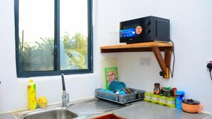 A kitchen with a sink, a window, a microwave, and various kitchen items on the counter. - Charming 1-bedroom apartment in enchanting Jambiani with AC (Jambiani)