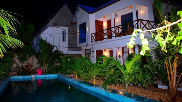 Un edificio de dos pisos con piscina, rodeado de plantas tropicales.