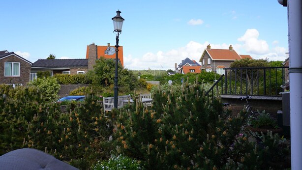A residential area with houses, a street lamp, and a variety of plants. - Bright 2-room studio with a view, private bathroom, kitchen, and a spacious, sunny balcony (Bergen aan Zee)