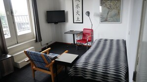A room with a bed, a chair, a table, a TV, and a radiator. - Bright 2-room studio with a view, private bathroom, kitchen, and a spacious, sunny balcony (Bergen aan Zee)