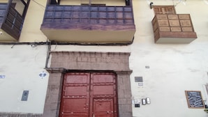 A red double door with metal studs, a stone base, and a balcony with a wooden railing. - SAPHY APARTAMENTS INN MINUTES AWAY FROM THE PLAZA DE ARMAS (Cusco)