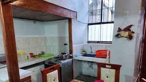 A compact kitchen with a gas stove, sink, and tiled backsplash. There is a dining table with chairs and a decorative item on the table. - SAPHY APARTAMENTS INN MINUTES AWAY FROM THE PLAZA DE ARMAS (Cusco)