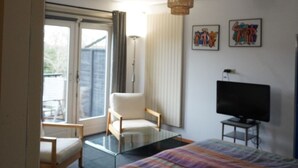 A hotel room with a bed, a chair, a television, and artwork on the wall. - Sunny Seaside Getaway: A Short Walk to Beach and Dunes (Bergen aan Zee)