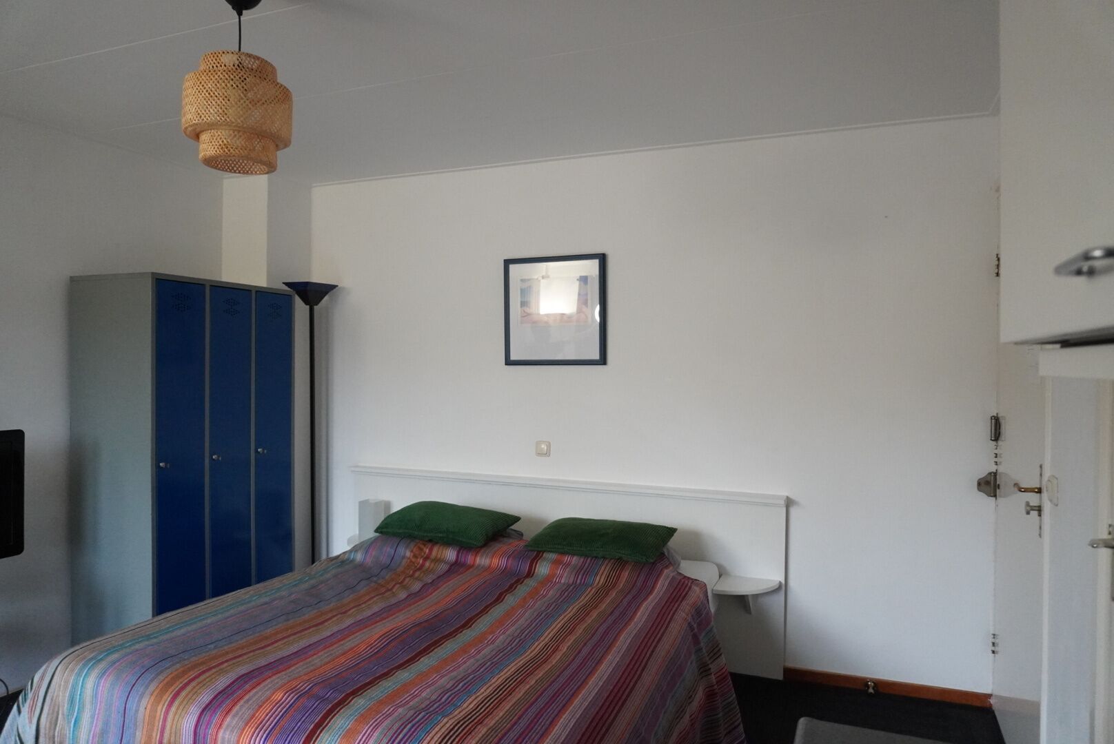 Une chambre à coucher avec un lit, une armoire, un tableau au mur et un luminaire suspendu.