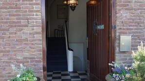 A brick building entrance with a wooden door, a black and white checkered floor, and two potted plants on either side. - Sunny Seaside Getaway: A Short Walk to Beach and Dunes (Bergen aan Zee)