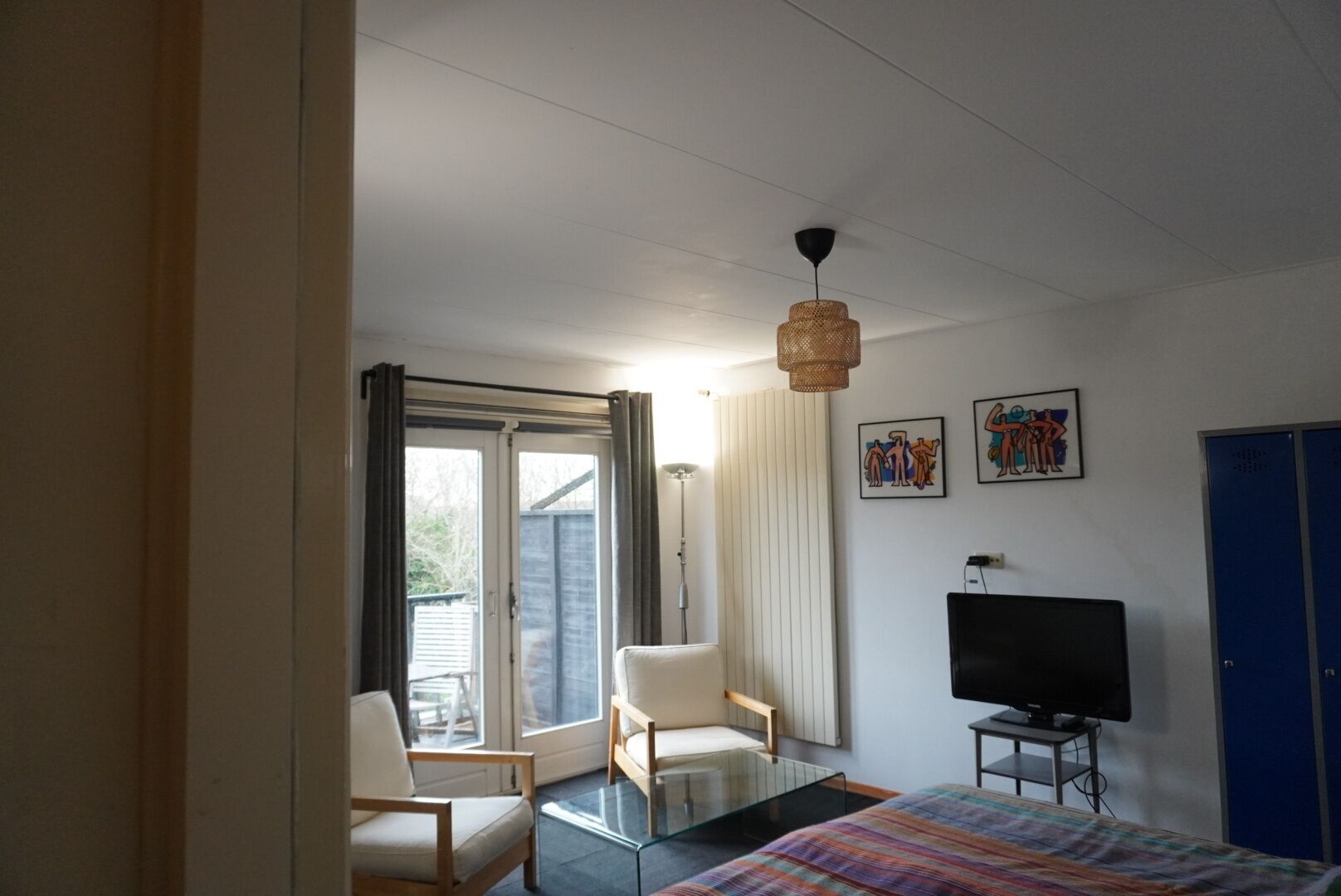 Une chambre d’hôtel comprenant un lit, une télévision, une table basse en verre, deux chaises, un bureau et une grande fenêtre avec des rideaux.
