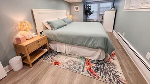 A bedroom with a bed, bedside table, lamp, and a rug. - Sandy Bottom | 2bd/1bt | 4 min walk to beach (Ventnor City)