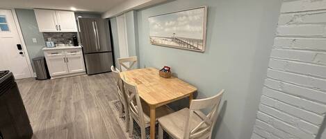 Un coin repas avec une table et des chaises en bois, une cuisine en arrière-plan et une décoration murale sur le thème de la plage.