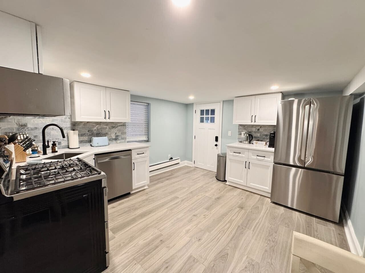 A modern kitchen with white cabinets, stainless steel appliances, and a light wood floor.