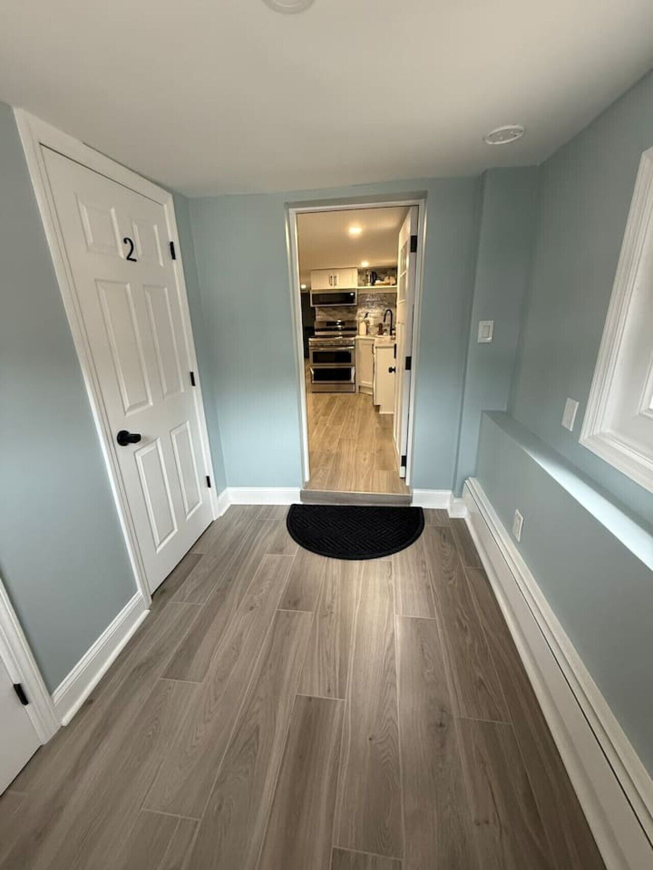 A hallway with a wooden floor, a black doormat, and a door with a number.