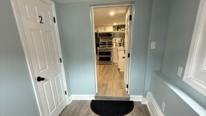 A hallway with a wooden floor, a black doormat, and a door with a number. - Sandy Bottom | 2bd/1bt | 4 min walk to beach (Ventnor City)