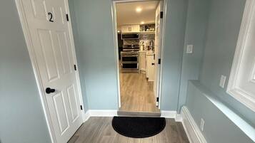 A hallway with a wooden floor, a black doormat, and a door with a number.