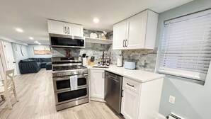 A modern kitchen with white cabinets, stainless steel appliances, and a grey tiled backsplash. - Sandy Bottom | 2bd/1bt | 4 min walk to beach (Ventnor City)