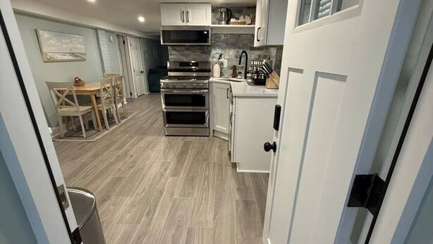 A compact kitchen with built-in appliances, a dining area with a table and chairs, and a trash bin. - Sandy Bottom | 2bd/1bt | 4 min walk to beach (Ventnor City)