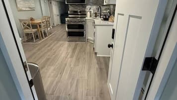 A compact kitchen with built-in appliances, a dining area with a table and chairs, and a trash bin.
