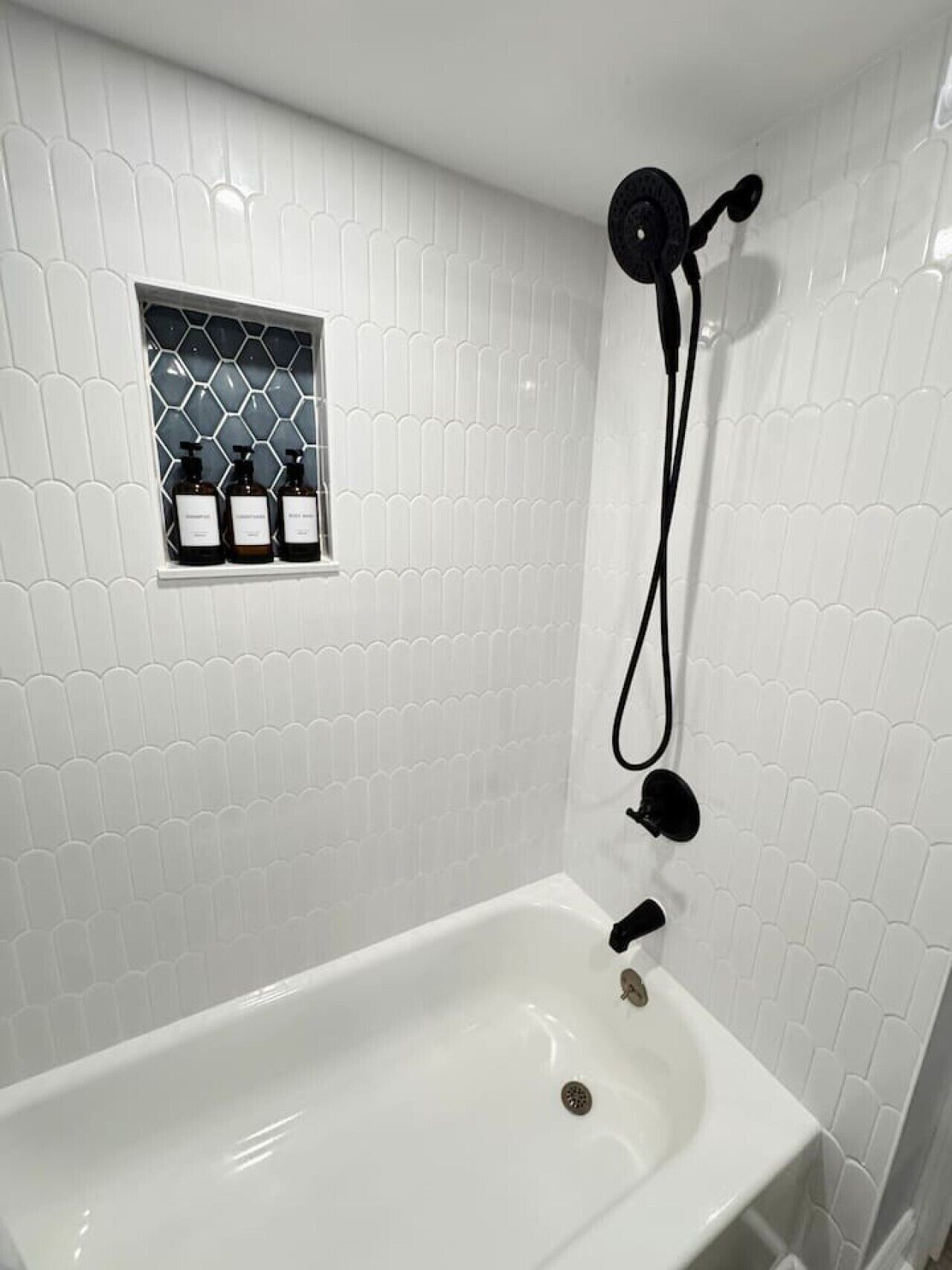 A bathroom with a white bathtub, a shower head, and a small shelf with toiletries.