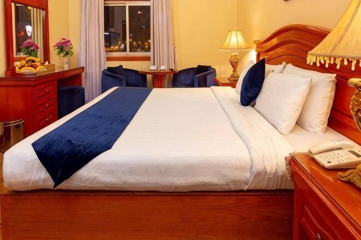 A hotel room with a large bed, bedside tables, a desk, and a window.