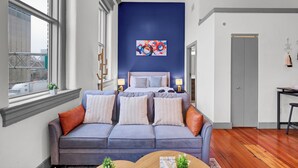 Un dormitorio moderno con una cama grande, una pared azul decorativa, un armario gris y una ventana con vistas a la ciudad.